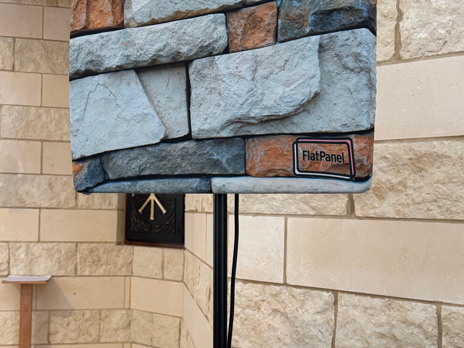 A DML500 flat panel speaker wearing an acoustically transparent stone print cover against a limestone wall