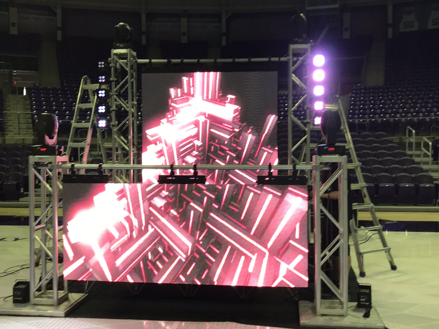 An LED wall and truss build going up on an arena floor with the seating bowl empty behind it