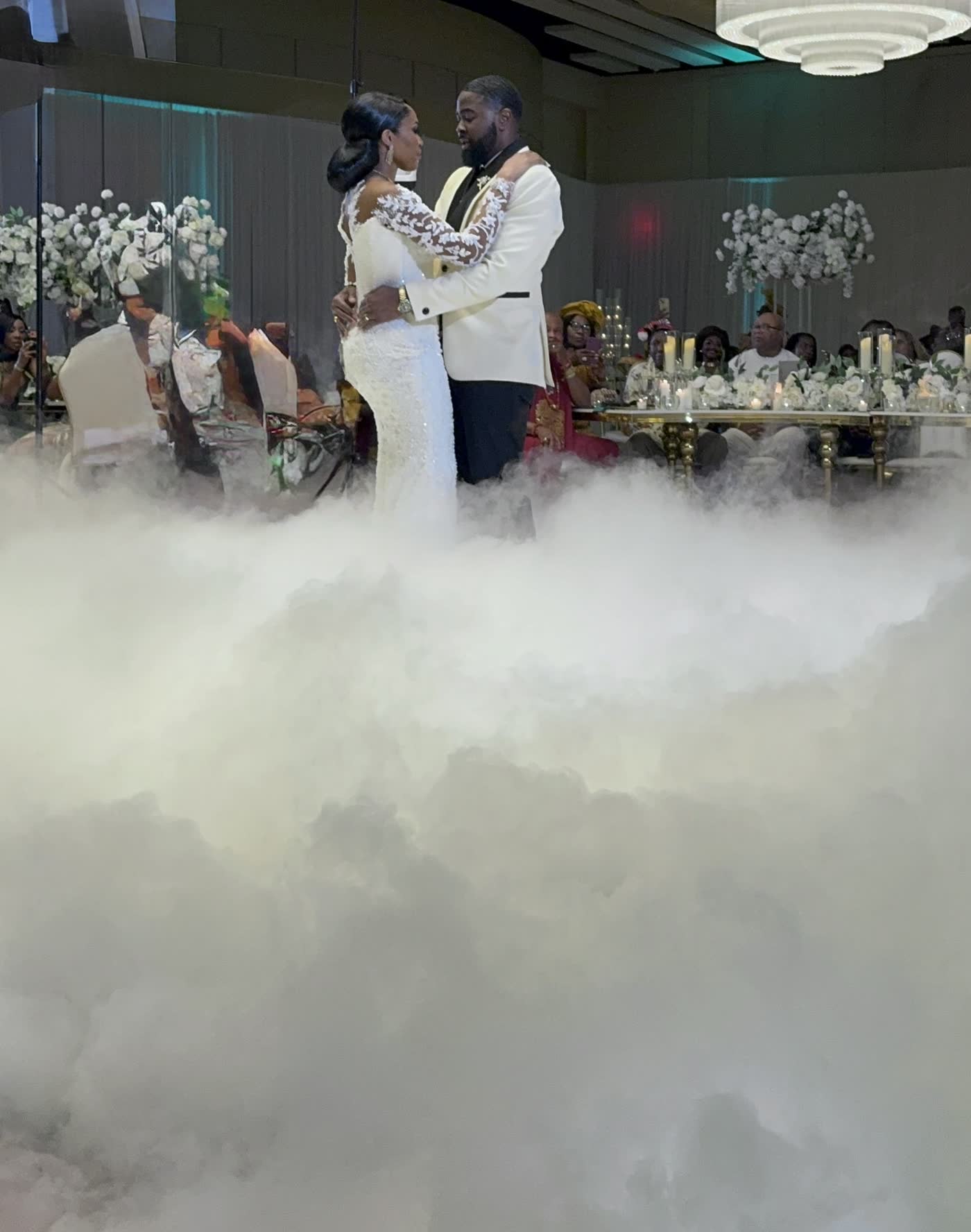 Couple standing above a deep bank of low lying fog on a hotel ballroom dance floor with the head table behind them