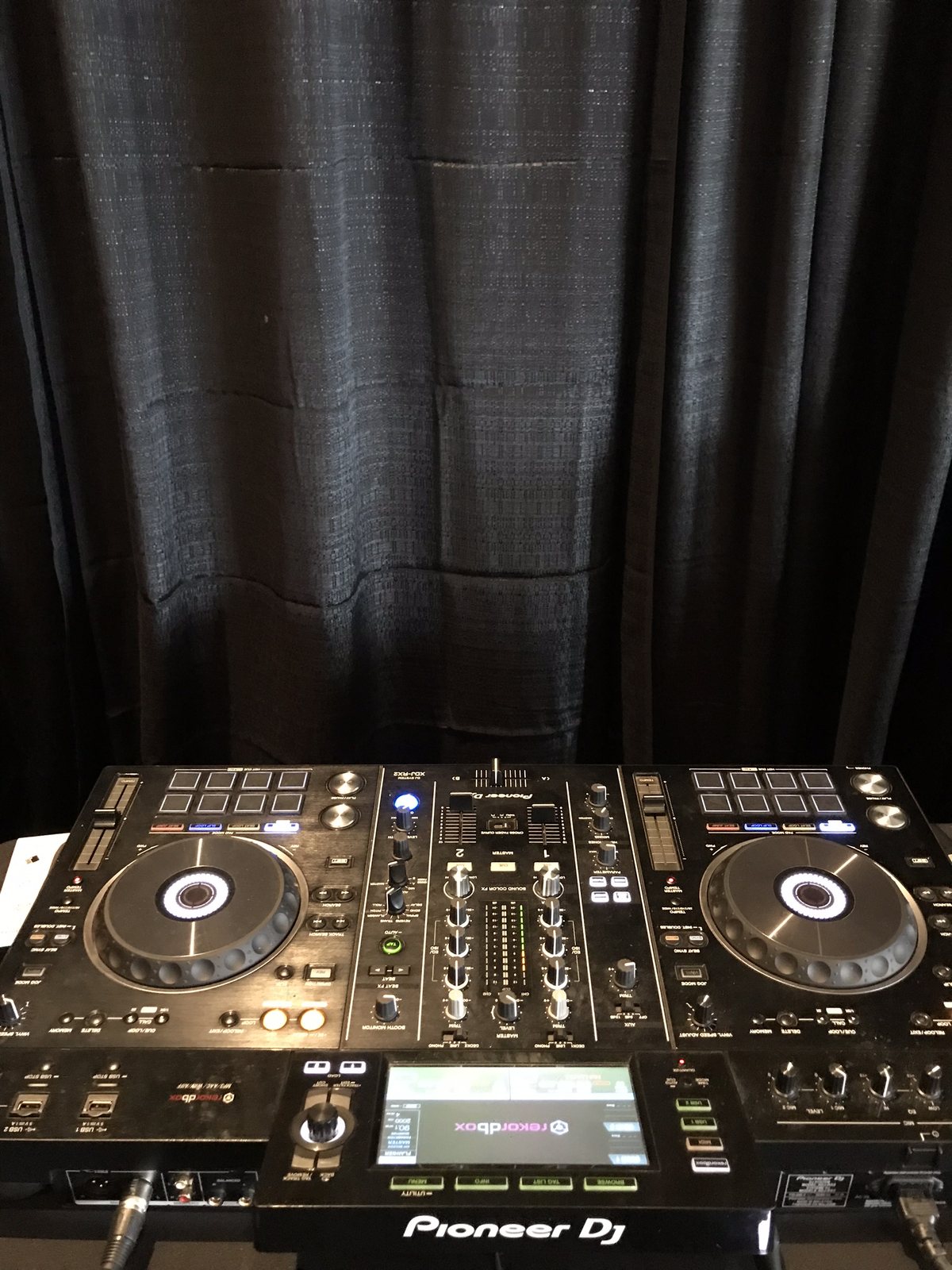 A pair of Pioneer DJ media players and a mixer set up on a black draped booth