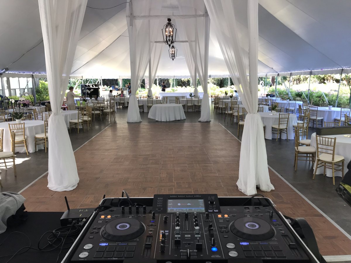 A DJ controller on a booth looking down the aisle of a draped tent reception