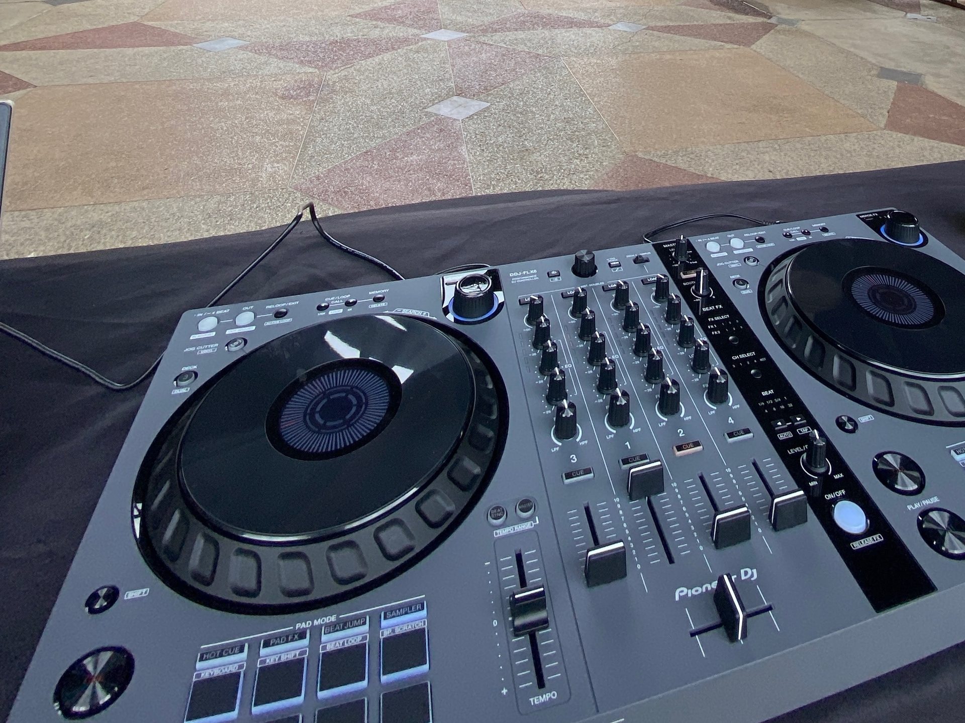A Pioneer DJ DDJ-FLX6 controller on a draped table under a stone park pavilion in Dallas
