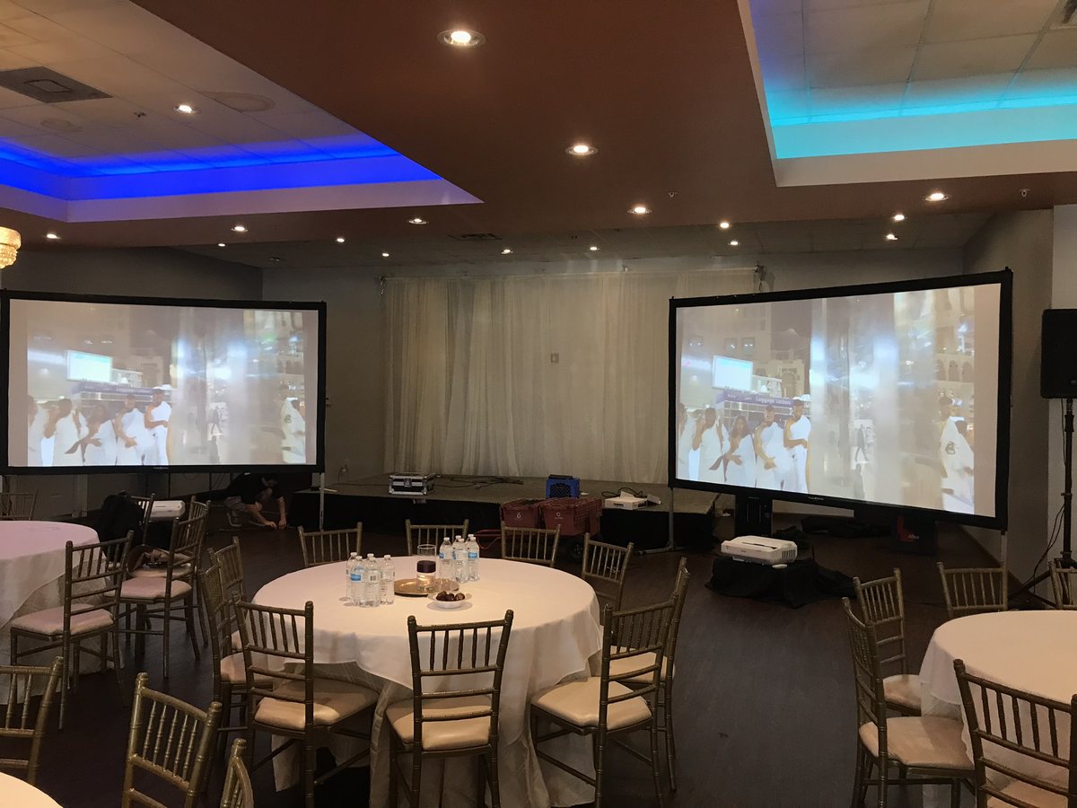 Two projection screens either side of a banquet room set with round tables