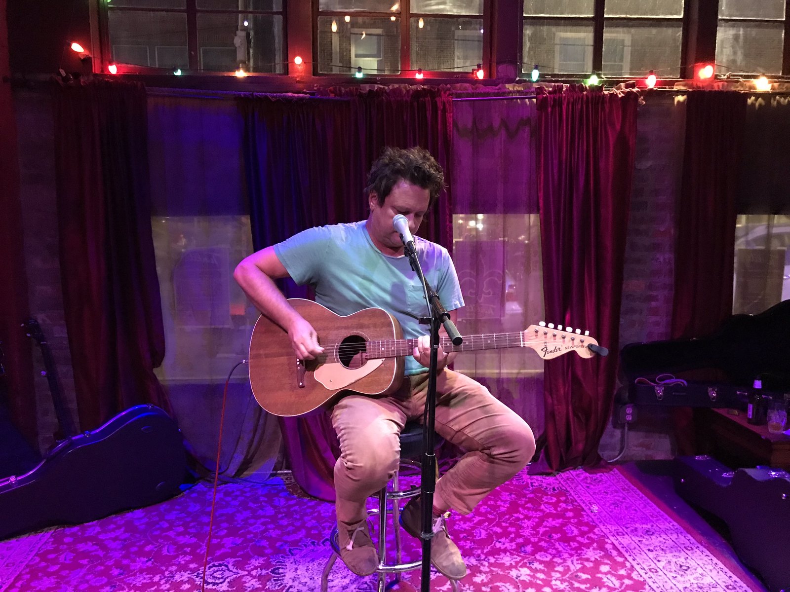 A solo performer on a small stage lit magenta with red drapes behind