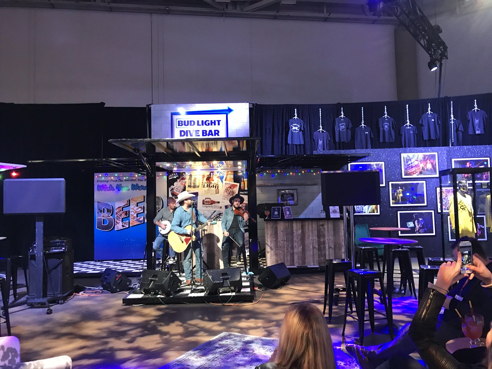 A band playing on a built stage inside a branded activation, with screens and truss above the room