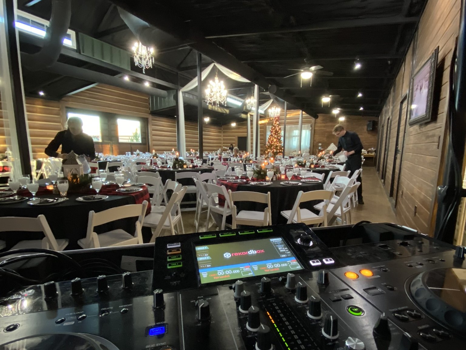 A DJ controller on a booth looking out over a barn venue with chandeliers and guests at tables