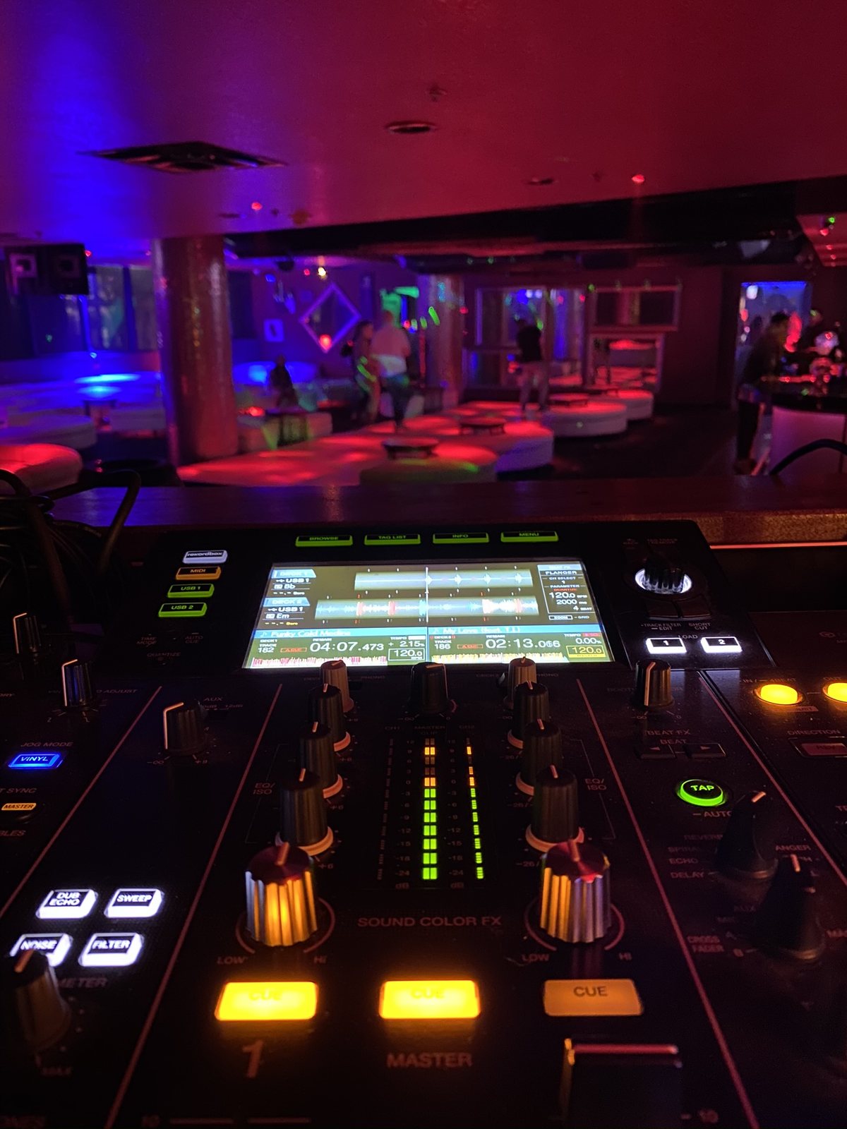 A DJ mixer and media players lit red and blue in a dark club room