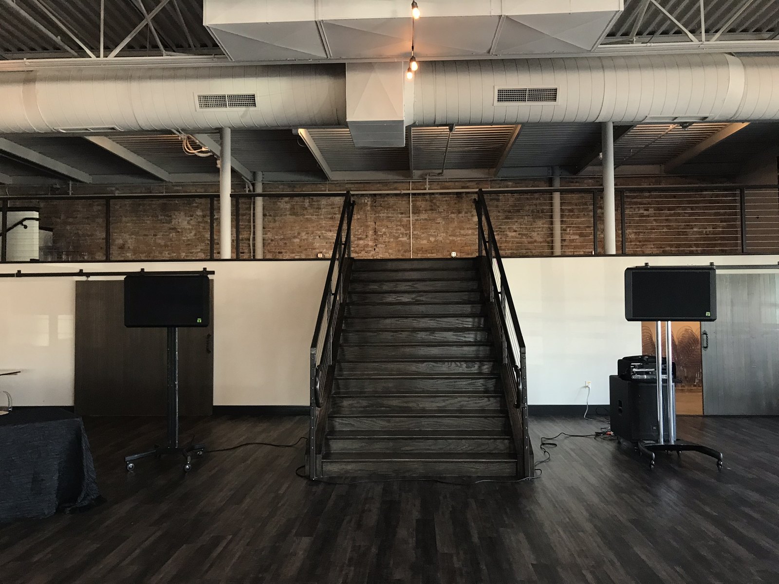 Two speakers on stands either side of a staircase in an empty event room before doors