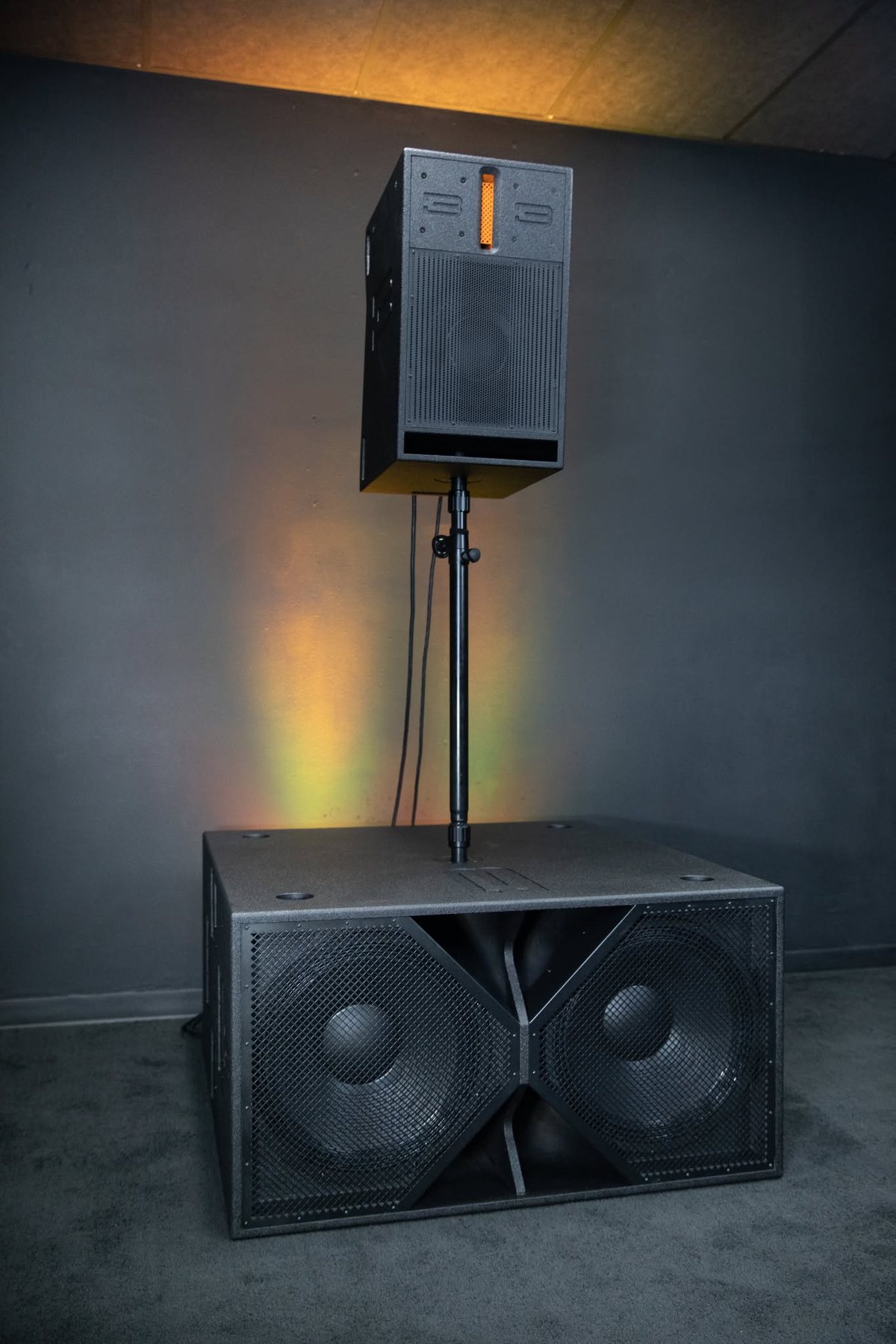 A speaker top on a pole above a dual eighteen inch subwoofer against a gray wall