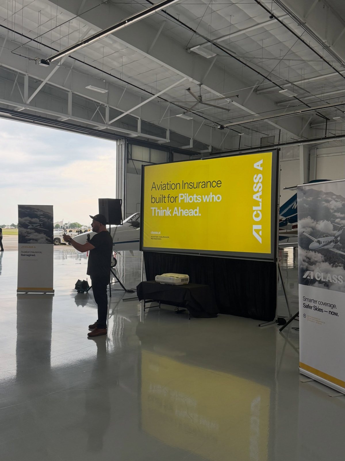 A freestanding projection screen showing a title slide in a large open space with a banner beside it