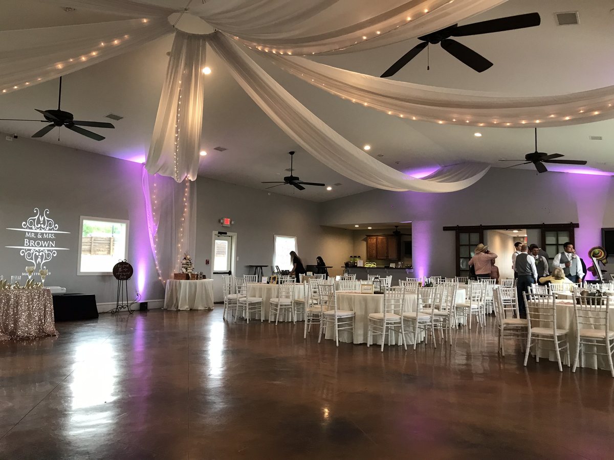 Pink uplighting around a draped reception room with round tables and an open floor