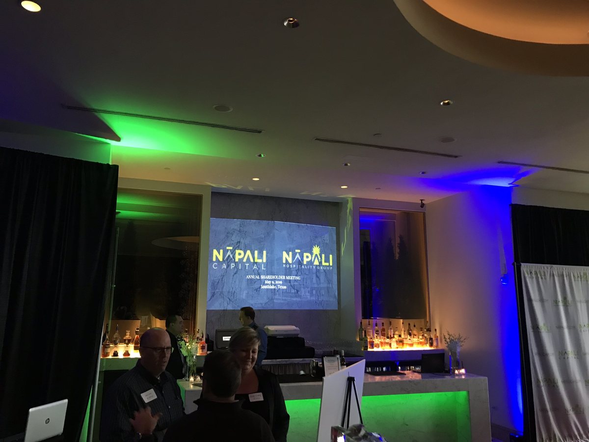 Green and blue uplighting along a room wall with a branded slide on the screen behind the guests