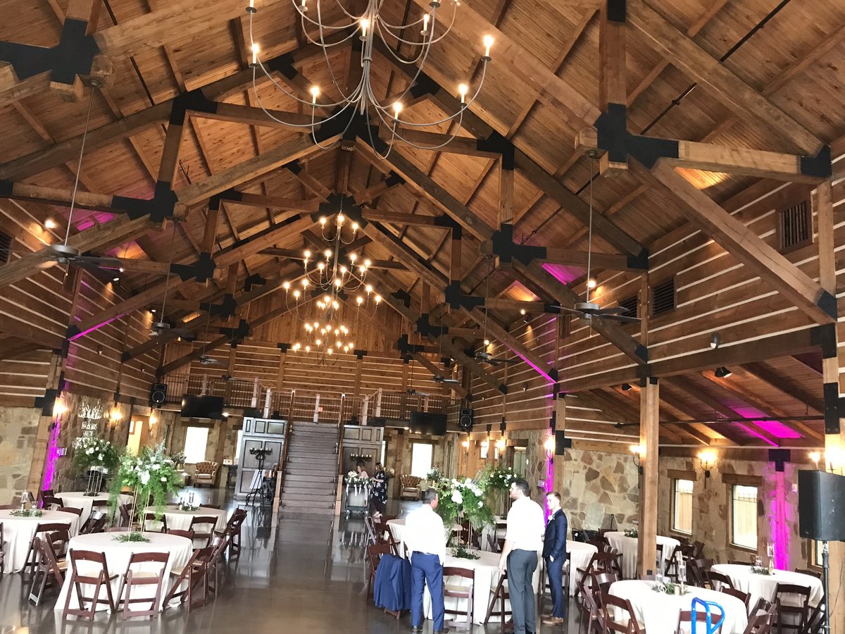 Pink uplighting along the walls of a wooden barn venue with chandeliers and tables set