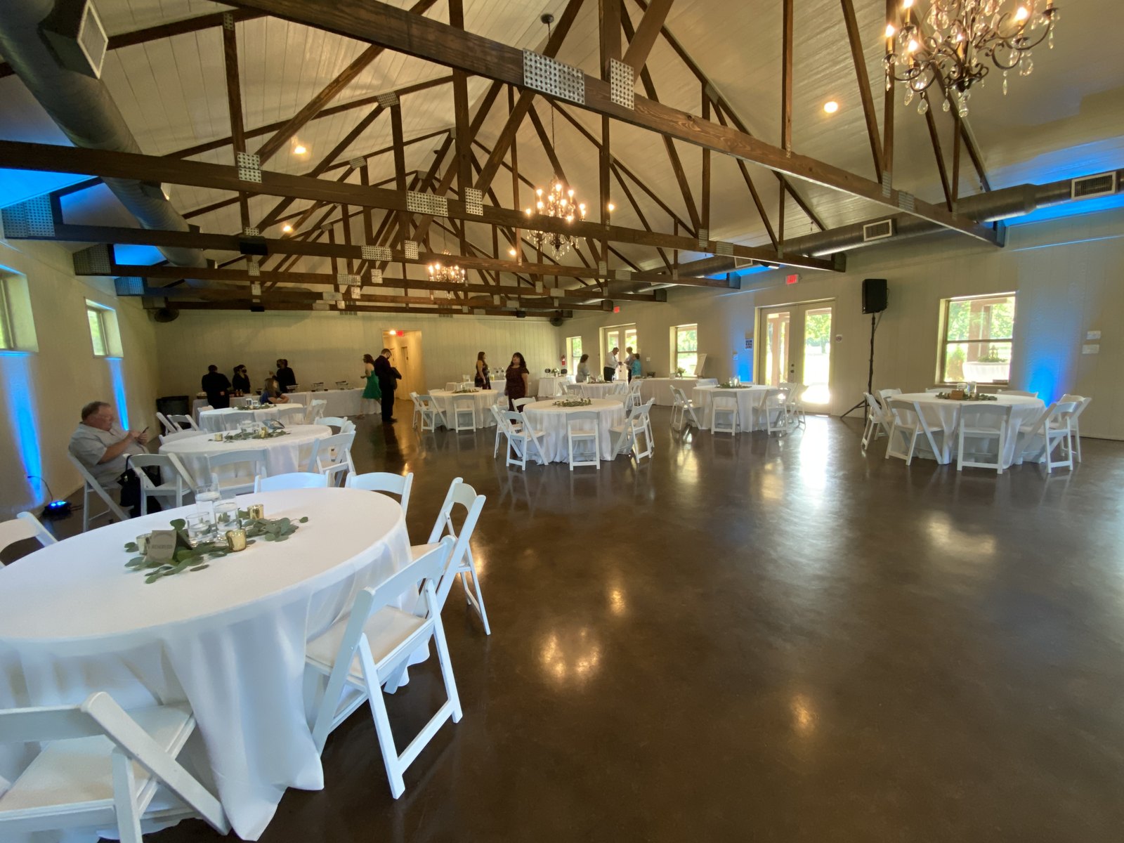 Blue uplighting along the walls of a white truss barn set with round tables