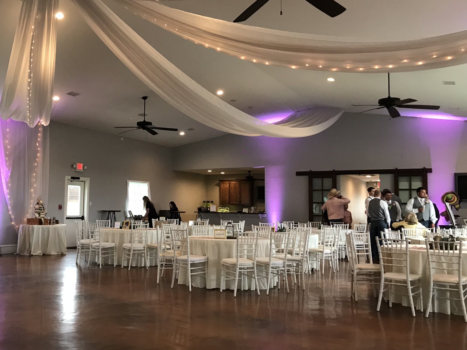 Violet uplighting behind draped ceiling fabric and string lights above a reception floor
