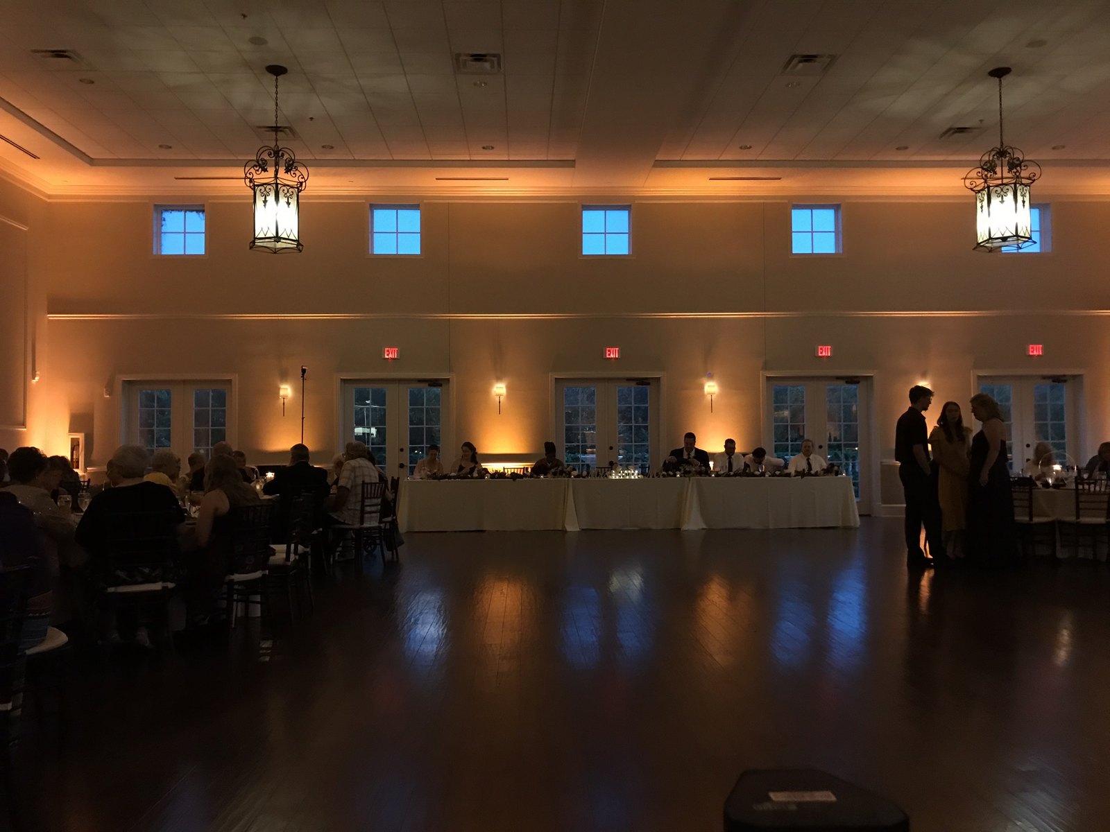 Warm amber uplighting between the windows of a hall lit by hanging lanterns