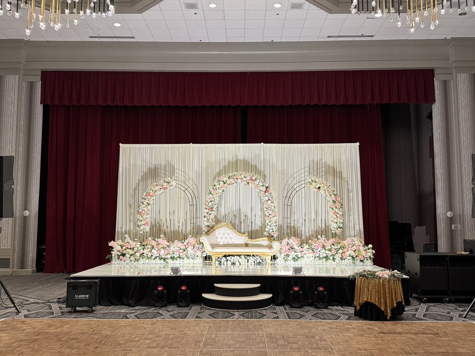 A long head table below a floral arch with speaker columns either side of the reception stage